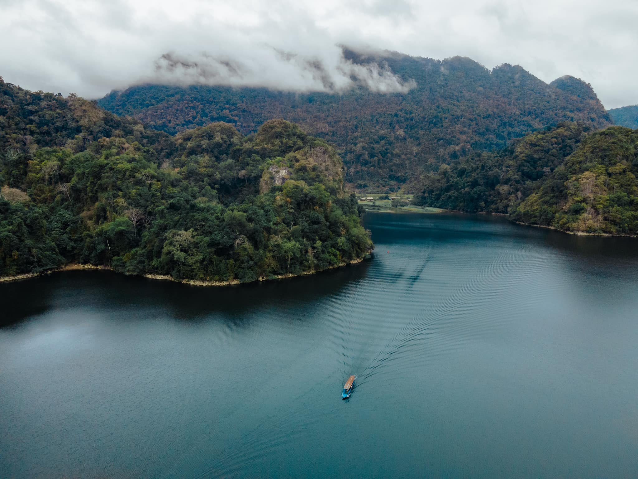 Morning boat cruise on Ba Be Lake, surrounded by misty mountains and calm waters.
